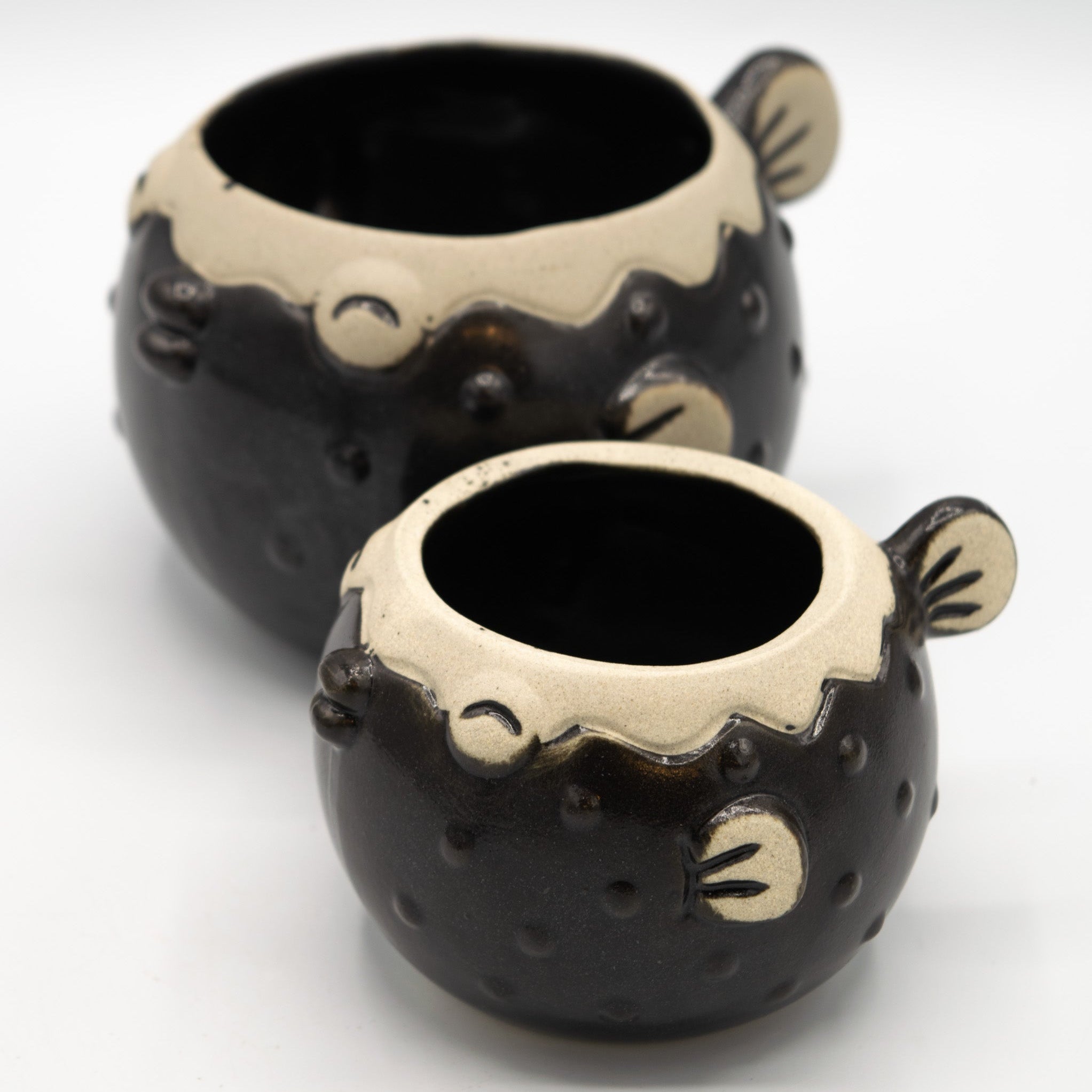 Two black ceramic pots with beige accents on a white background