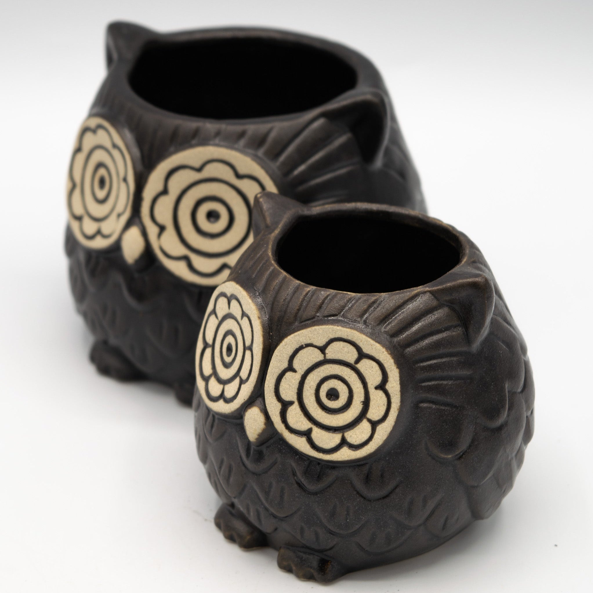 Two black owl-shaped planters with beige circular patterns on a white background